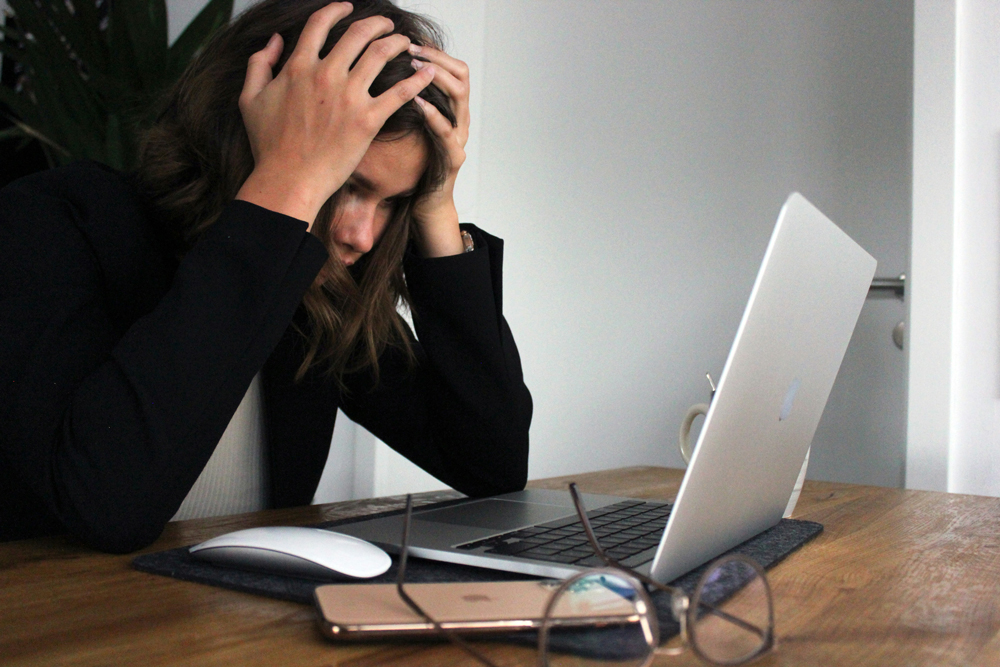 A person sitting in front of a laptop and holding their head in frustration