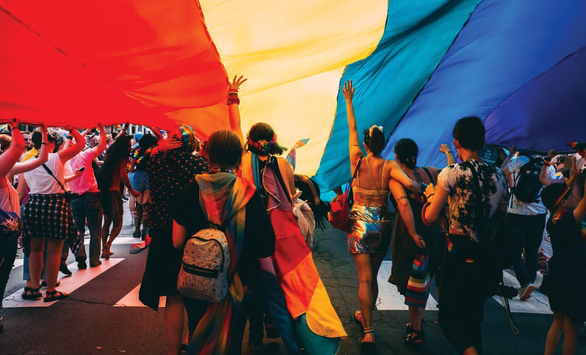 a large rainbow flag with a crowd of people underneath