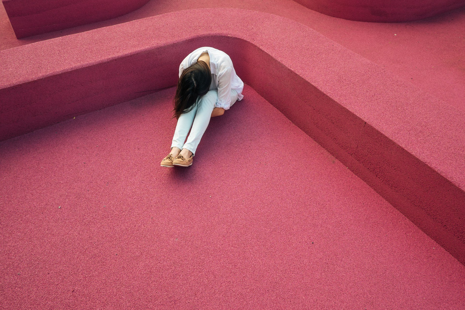 a high angle shot of a woman sitting with forehead on her knees