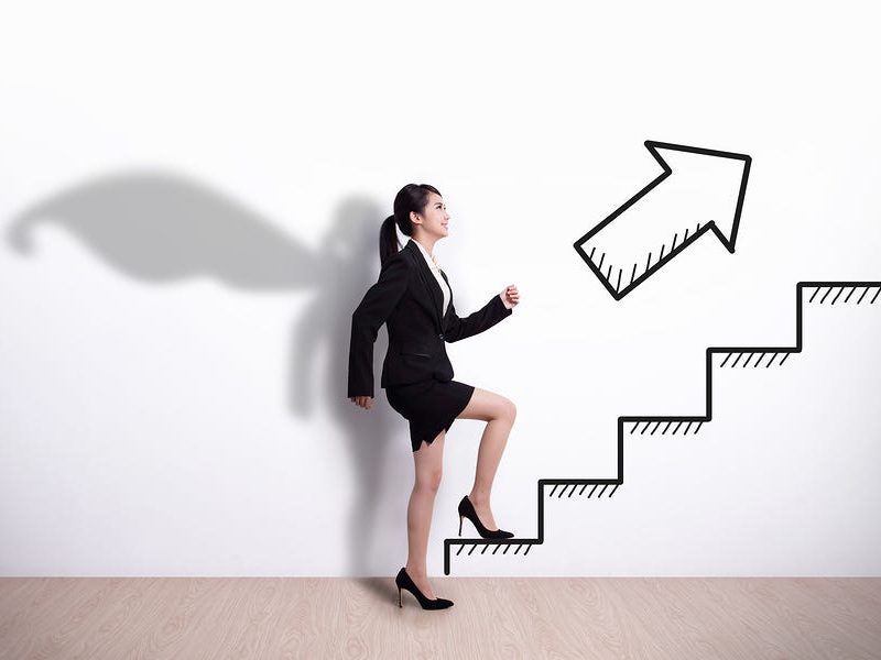 A women in office attire climbing stairs with her shadow wearing a cape